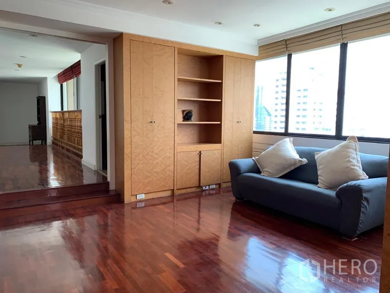 Condominium for sale in Khlong Toei, Bangkok - Cozy lounge with built-in wood cabinets, sofa and large windows on polished floors.