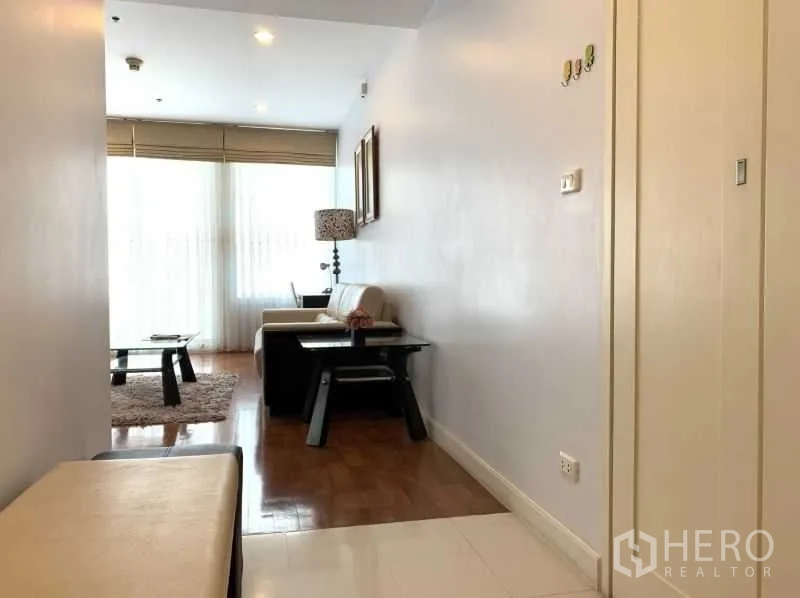 Condominium for rent in Khlong Toei, Bangkok - Hallway opening to a sunlit lounge with sheer curtains and floor‑to‑ceiling windows.