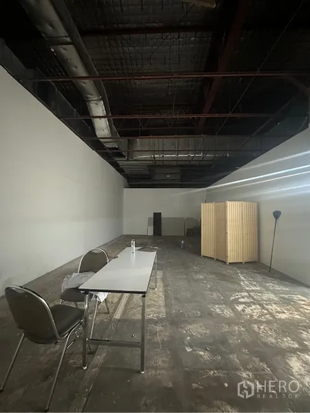 Retail Space for rent - Deep open-plan retail interior with high exposed ceiling, ducting, and unfinished flooring.