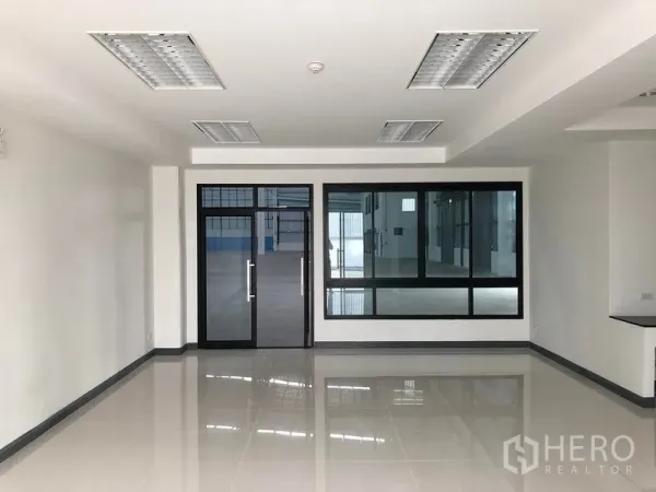 Factory for rent in Samut Prakan - Spacious white office room with recessed lighting and glass partition to the production area.