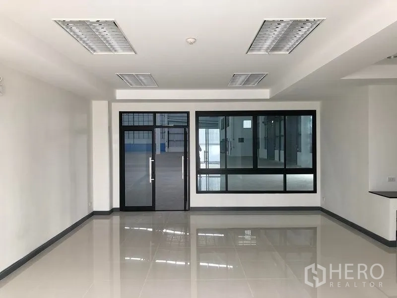 Factory for rent in Samut Prakan - Spacious white office room with recessed lighting and glass partition to the production area.