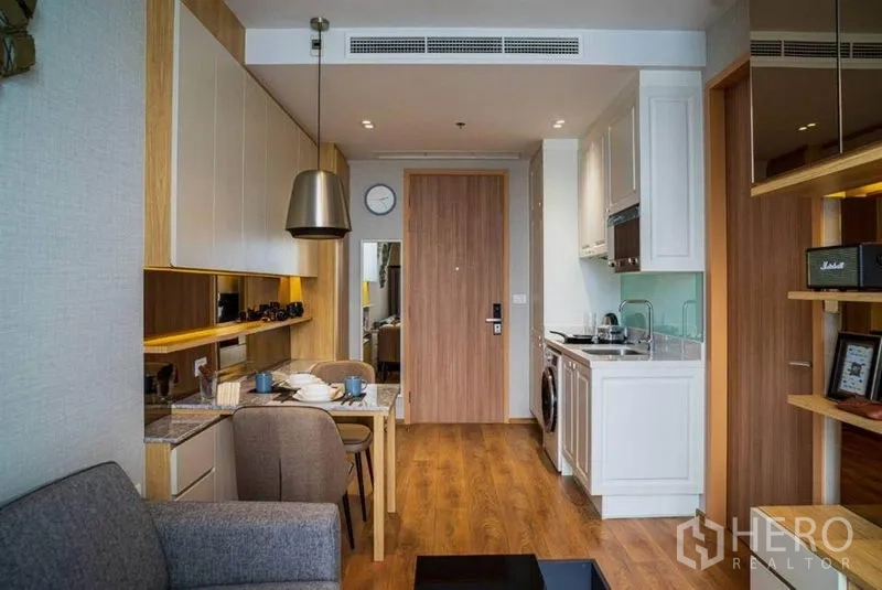 公寓 出租在Watthana, Bangkok - 从入口望向室内的小厨房与餐桌，木地板、内置收纳与层架一应俱全。