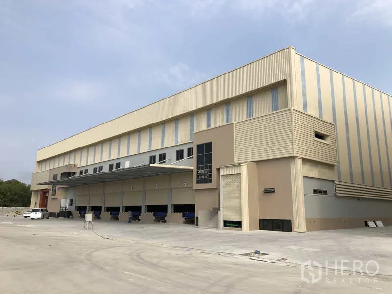 Factory for rent or sale in Samut Prakan - Modern factory exterior with multiple dock-level loading bays, canopy, and a wide concrete yard.