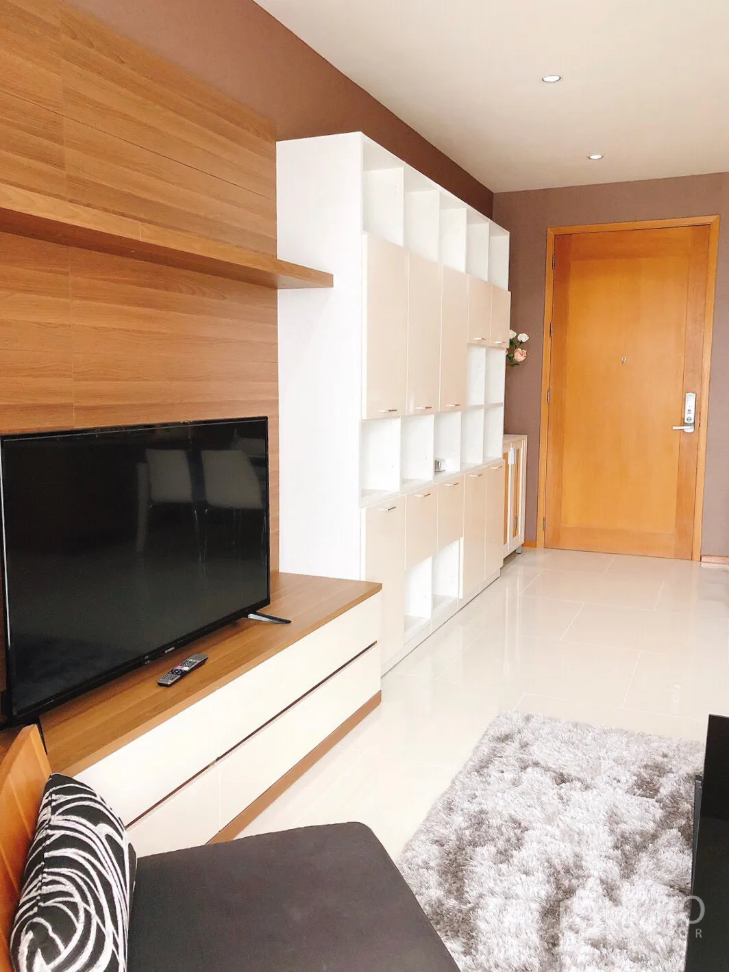 Condominium for rent in Khlong Toei, Bangkok - TV wall with wood paneling, white cabinets and entrance door in a modern condo.