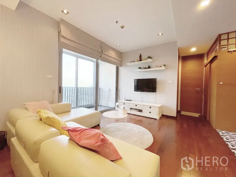 Condominium for sale in Khlong Toei, Bangkok - Bright living room with cream sectional sofa, wall-mounted TV and sliding doors to a balcony.