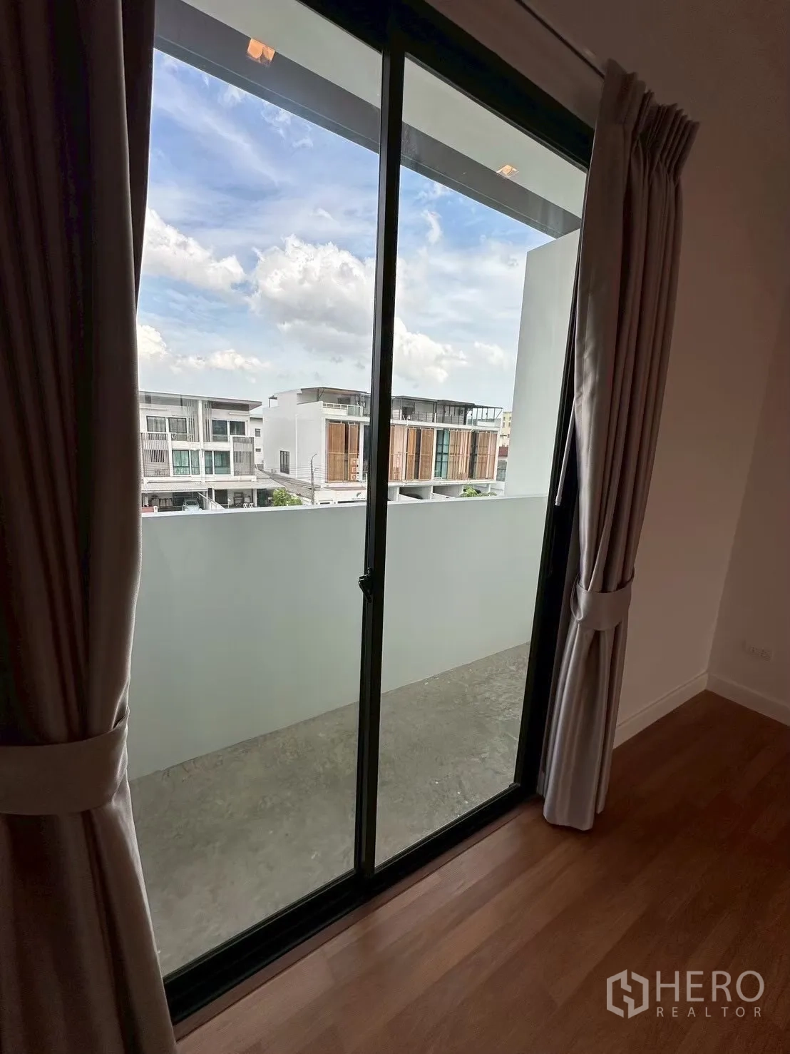 Home Office for rent in Lat Phrao, Bangkok - Bedroom sliding glass door opening to a small balcony with neighborhood view and curtains.