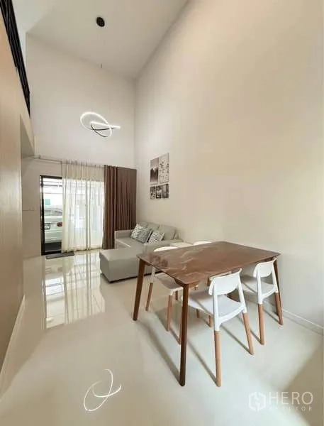 Townhouse for rent in Bang Phli, Samut Prakan - Dining area with wooden table, high ceilings and sheer curtains at the front door.