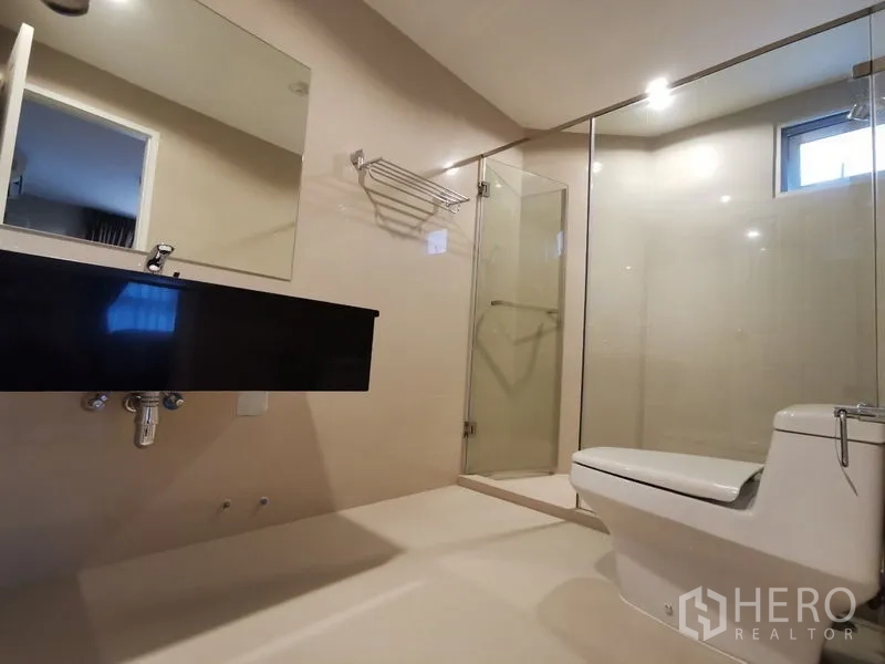 Condominium for rent or sale in Huai Khwang, Bangkok - Bright bathroom with glass shower, wall-mounted black vanity, and toilet in a modern Huai Khwang condo.