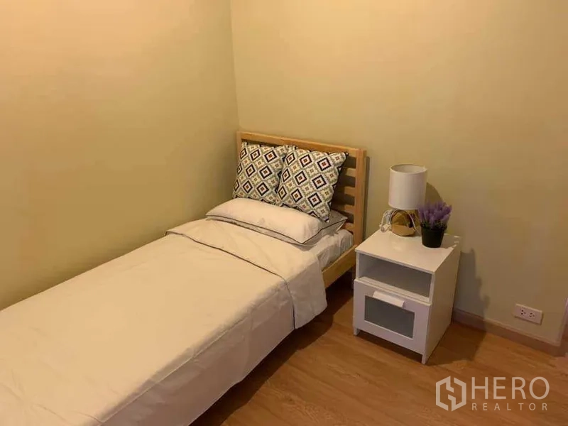 公寓 出租在Watthana, Bangkok - 次卧配单人床、白色床品与床头柜台灯，木地板。