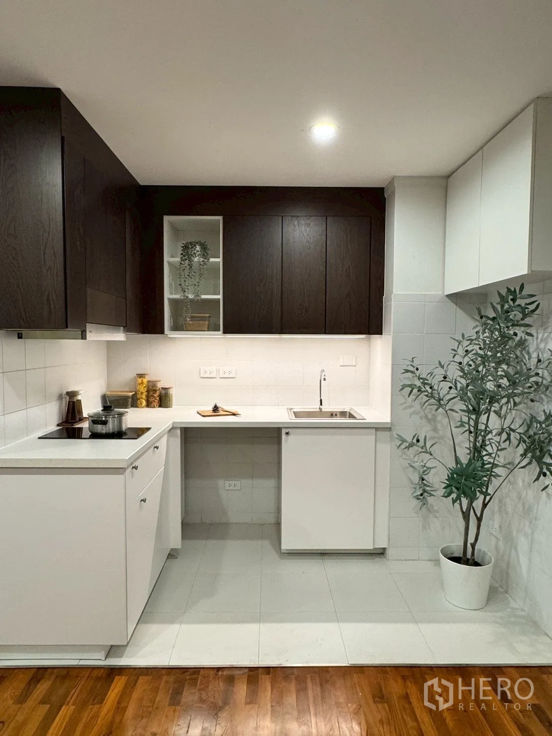 公寓 for sale in Watthana, Bangkok - 小型L形厨房，深木色橱柜、白色台面、电磁炉与水槽。