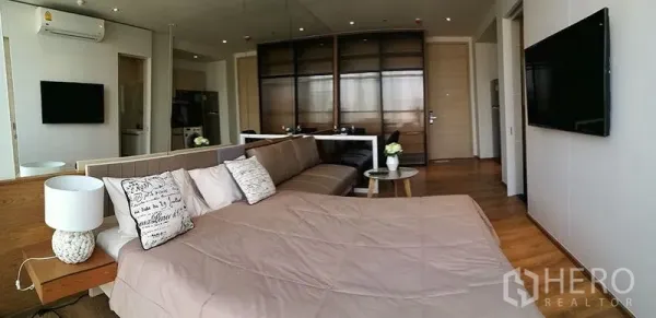 Condominium for sale in Khlong Toei, Bangkok - Open-plan bedroom featuring a sofa, mirrored wall, wood flooring and TV.