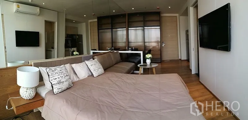 Condominium for sale in Khlong Toei, Bangkok - Open-plan bedroom featuring a sofa, mirrored wall, wood flooring and TV.