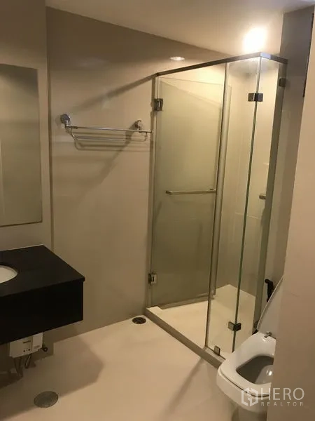Condominium for rent or sale in Huai Khwang, Bangkok - Modern bathroom with glass-enclosed shower, vanity counter and toilet.