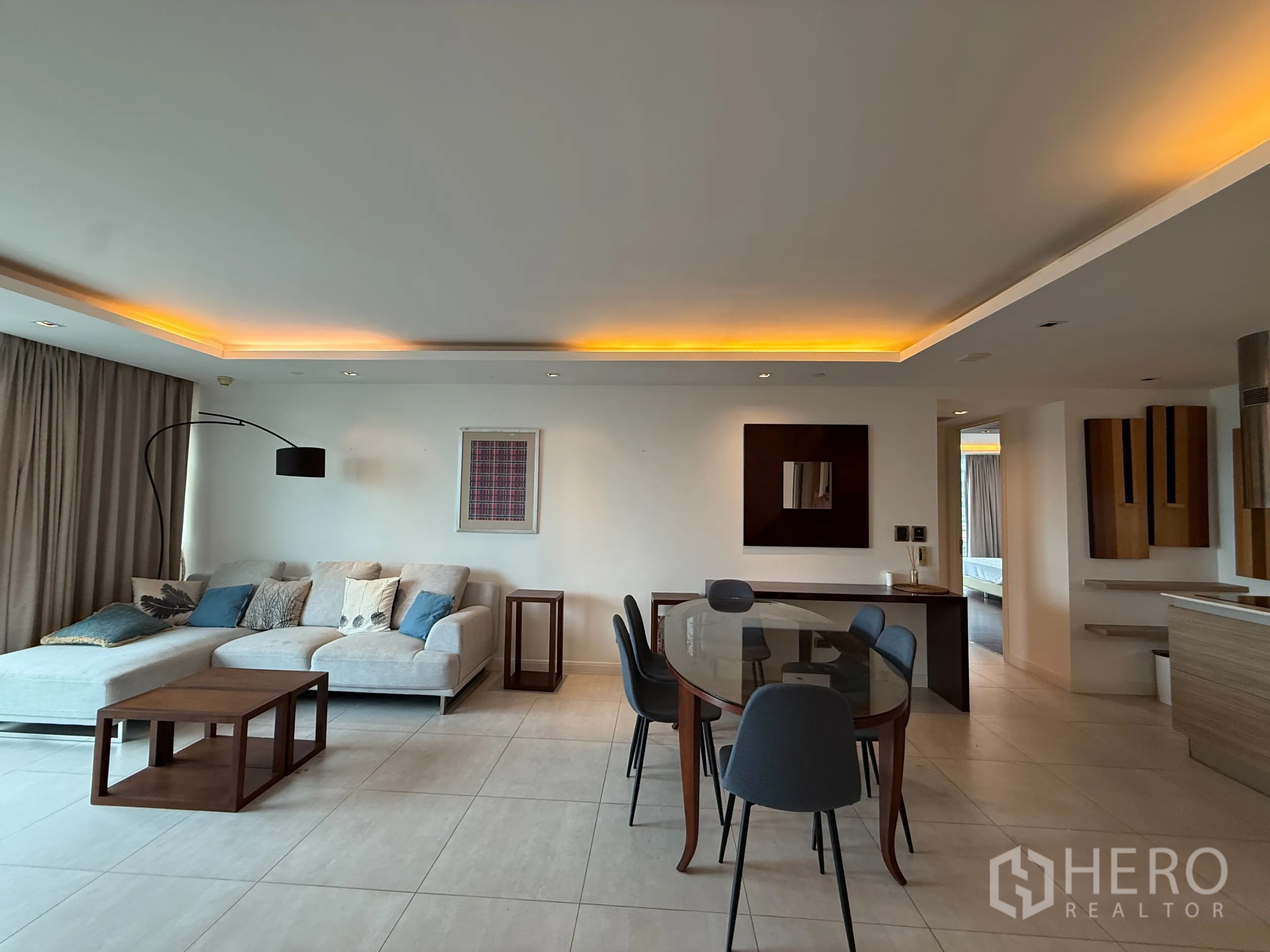 公寓 出租在Phaya Thai, Bangkok - 开放式客餐厅，吊顶氛围灯，转角沙发与玻璃餐桌。
