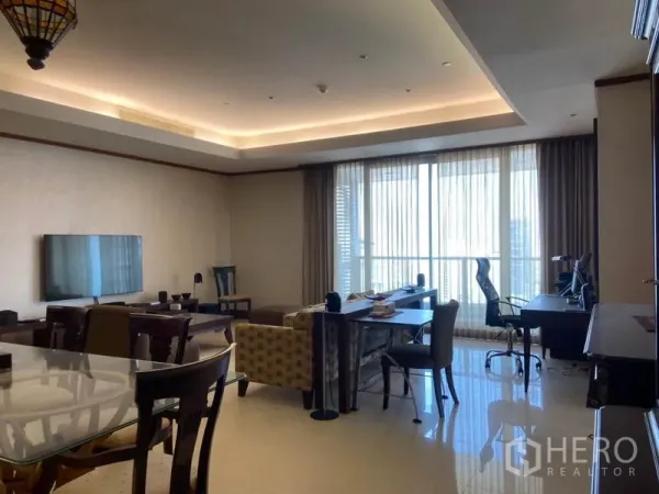 Condominium for rent in Sathon, Bangkok - Living area with TV, sofa and workstations facing floor-to-ceiling windows and balcony access under cove lighting.