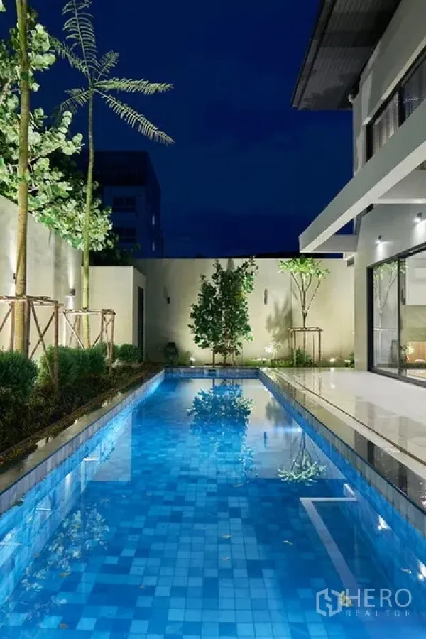 Detached House for rent in Watthana, Bangkok - Evening view of the illuminated lap pool with landscaped garden and modern boundary walls.