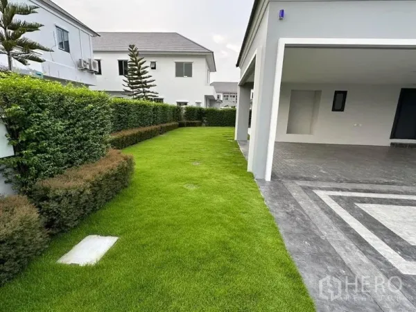 Detached House for sale in Lat Krabang, Bangkok - Side yard with lush grass beside a covered carport and gray tiled driveway.