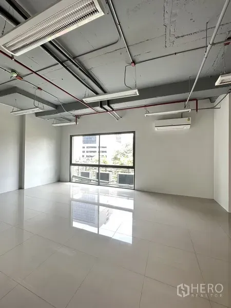 Office Space for rent in Khlong Toei, Bangkok - Light-filled corner of the office showing a large sliding window, wall-mounted AC and smooth tiled flooring.