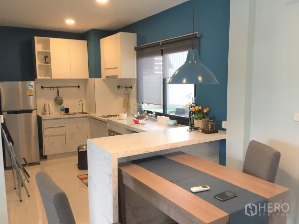 Townhouse for rent in Saphan Sung, Bangkok - Modern U-shaped kitchen with white cabinets, stone peninsula, pendant light and stainless fridge.