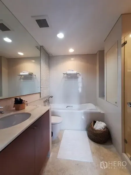 Condominium for rent or sale in Khlong Toei, Bangkok - Modern bathroom with vanity, large mirror, recessed lights, and a bathtub.