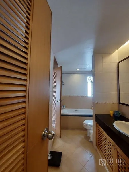 Apartment for rent - Warm-tone bathroom with bathtub, toilet, vanity and louvered wood cabinets.