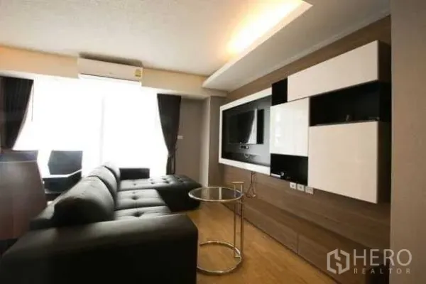 Condominium for rent in Khlong Toei, Bangkok - Living area with built-in TV wall, modern cabinetry and large window with blackout curtains.