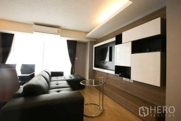 Condominium for rent in Khlong Toei, Bangkok - Living area with built-in TV wall, modern cabinetry and large window with blackout curtains.
