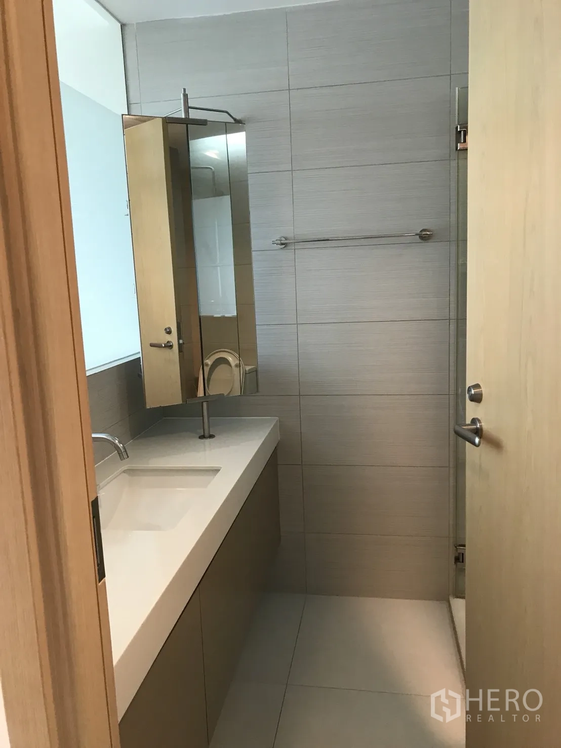 Condominium for rent in Khlong Toei, Bangkok - Contemporary bathroom with long vanity, mirror cabinet and glass shower enclosure.