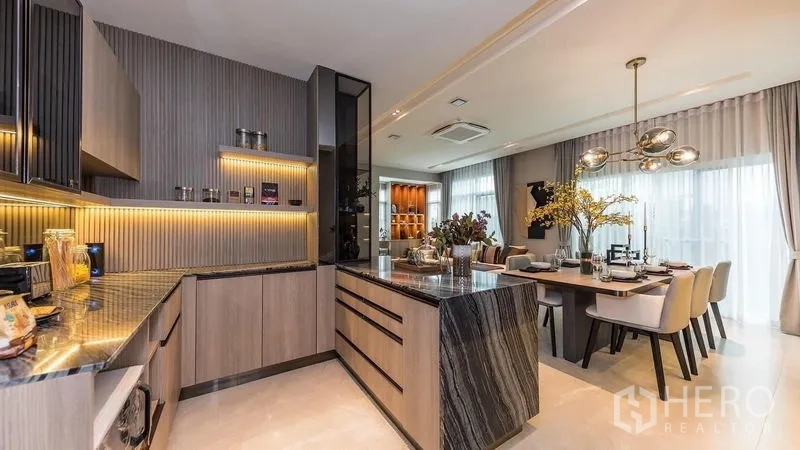 独立式住宅 出租在Prawet, Bangkok - U形厨房，石材中岛、木质橱柜与暖色灯带。