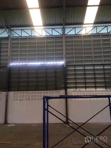 Warehouse for rent in Samut Prakan - Warehouse interior with high steel-truss roof, skylights and ventilated louvered side panels above a solid block wall.