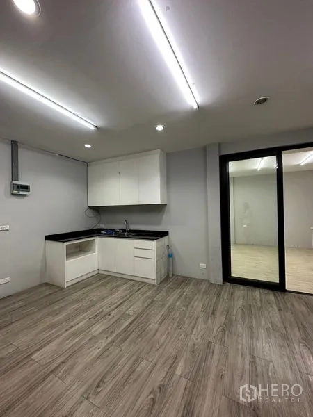 零售空间 出租在Khlong Toei, Bangkok - 紧凑的茶水间，白色橱柜与黑色台面，木纹地面，连接推拉玻璃门。