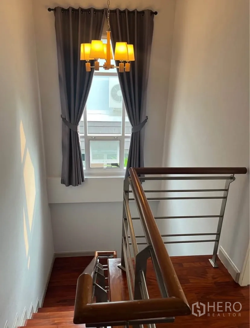 Detached House for rent or sale in Lat Phrao, Bangkok - Stairwell with wooden steps, stainless handrail, chandelier and curtained window.