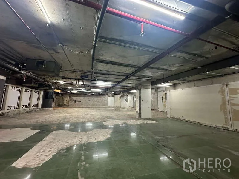 Retail Space for rent - Open-plan retail unit with central pillars, mixed green tile and concrete flooring, and sprinkler piping.