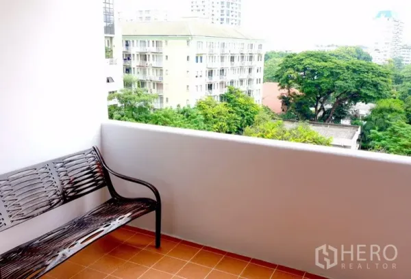 Condominium for rent or sale in Watthana, Bangkok - Covered balcony with bench overlooking greenery and nearby apartment buildings.