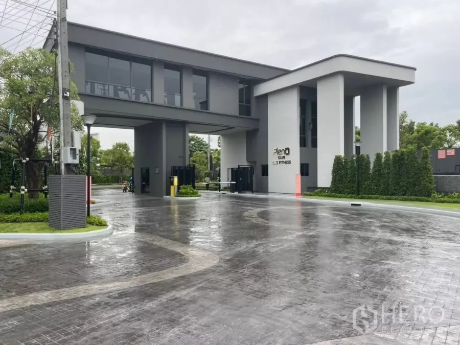 Townhouse for rent in Samut Prakan - Modern clubhouse entrance with security gate and Pleno Club Fitness signage on a rainy day.