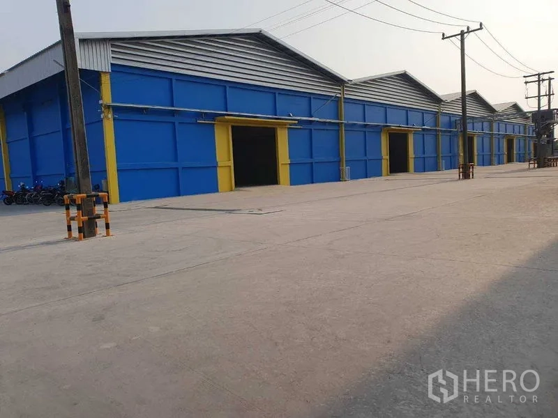 货栈 出租在Khlong Luang, Pathum Thani - 多联排蓝色仓库临宽混凝土车道，适合卡车通行与装卸。