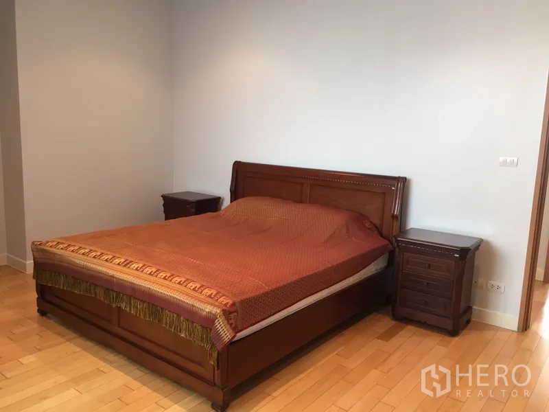 Condominium for rent in Khlong Toei, Bangkok - Large master bedroom featuring a wooden bed frame with matching nightstands and hardwood floors.