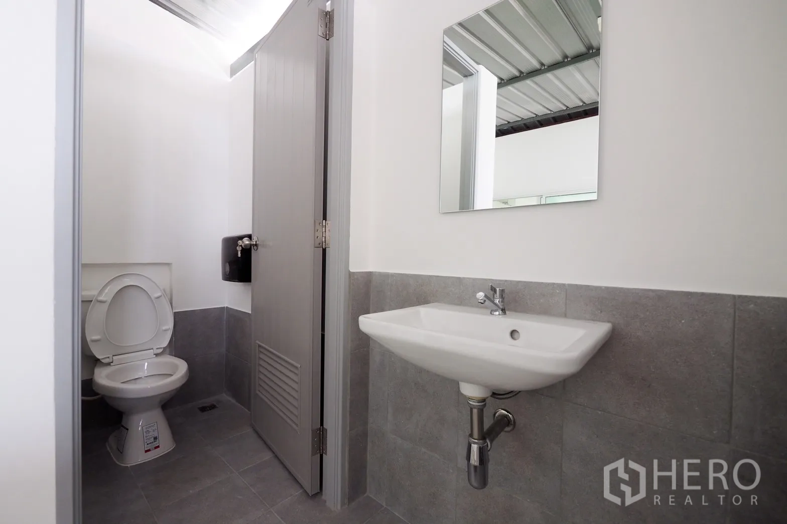 Office Space for rent in Khlong Toei, Bangkok - Clean modern restroom with gray tiles, toilet, wall-mounted sink and mirror.