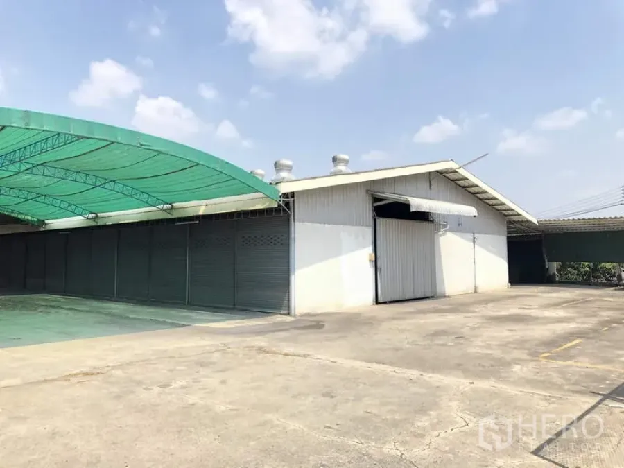 货栈 出租在Khlong Luang, Pathum Thani - 仓库外观，金属推拉大门、屋顶通风口与宽阔混凝土场地。