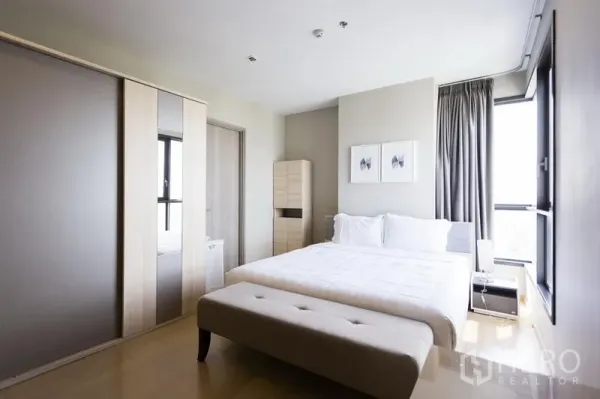 公寓 出租在Watthana, Bangkok - 第二卧室配白色床品、床尾长凳、推拉衣柜与转角采光窗。