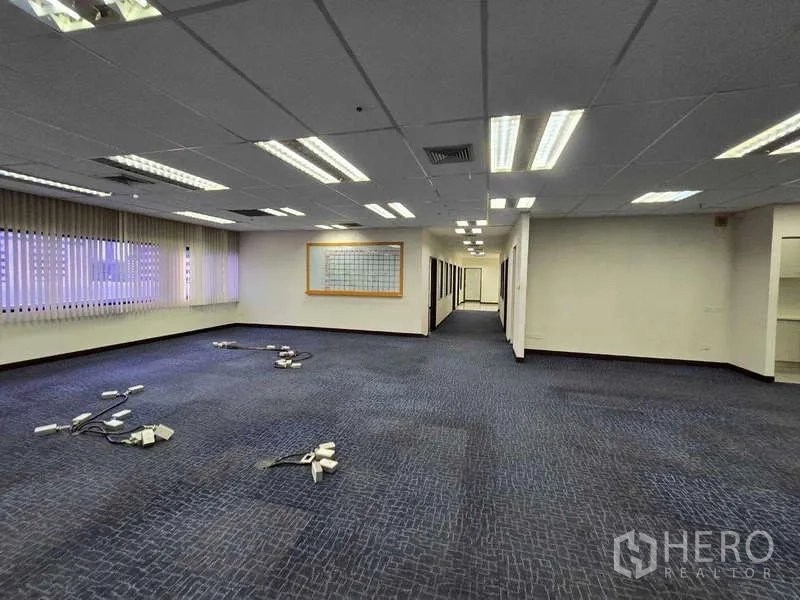 Office Space for rent in Khlong Toei, Bangkok - Large open-plan workspace with blue carpet, window blinds and fluorescent lighting.