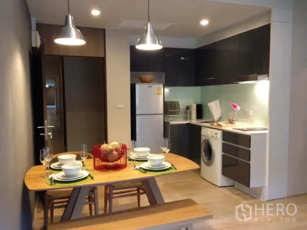 คอนโด ให้เช่าในWatthana, Bangkok - ครัวและพื้นที่ทานอาหารแบบเปิด ตู้หน้าบานเงา ตู้เย็น เครื่องซักผ้า และไฟแขวนเหนือโต๊ะ