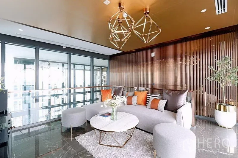 Condominium for rent in Watthana, Bangkok - Stylish lounge with geometric gold pendant lights, curved sofa and floor‑to‑ceiling windows.
