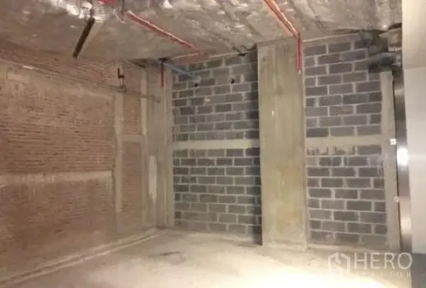 Retail Space for rent - Unfinished 76 sqm retail unit with exposed concrete ceiling, brick and block walls, and visible red piping.