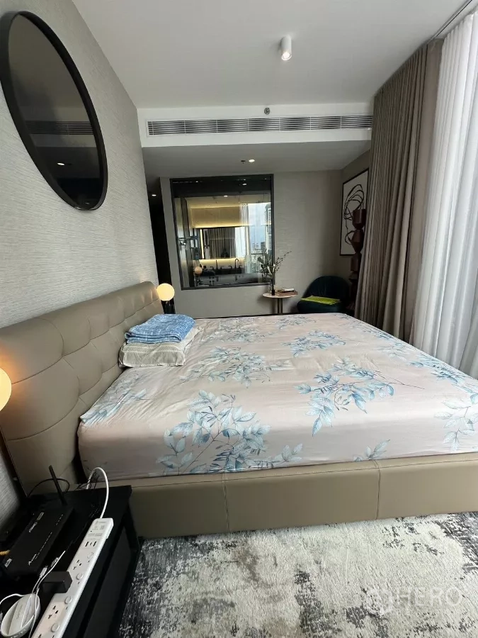 Condominium for rent in Bang Rak, Bangkok - Primary bedroom with upholstered bed, wide windows, and glass panel looking into the ensuite bathroom.