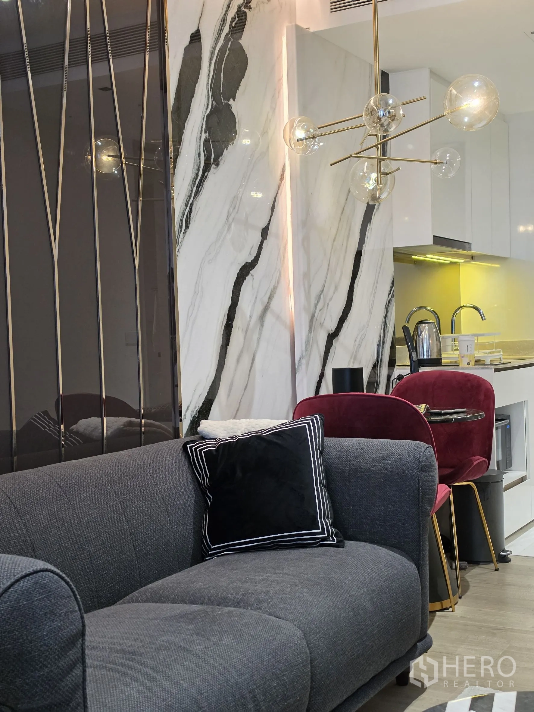 Condominium for rent in Khlong Toei, Bangkok - Cozy living room with gray sofa, marble accent wall, and modern chandelier over dining set.