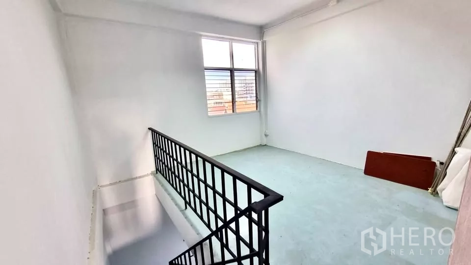 Townhouse for rent in Huai Khwang, Bangkok - Upper landing with window and black railing in a white-walled space.