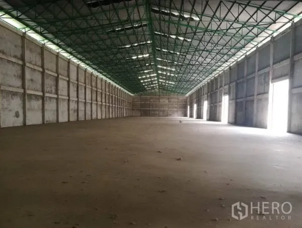 Warehouse for rent in Bang Sao Thong, Samut Prakan - Spacious warehouse interior featuring a high steel-truss roof with skylights and multiple side loading doors.