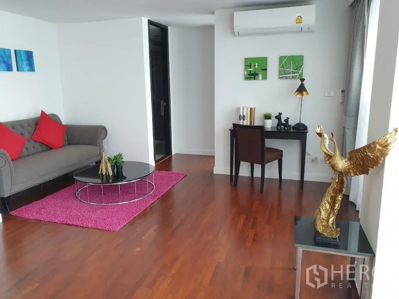 公寓 出租在Bang Rak, Bangkok - 次客厅，纽钉沙发、玫红地毯、书桌与金色装饰摆件。