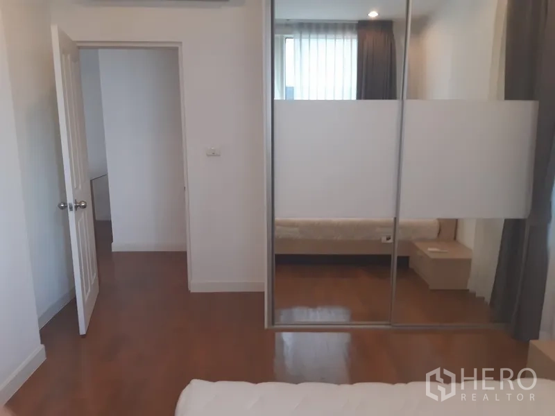 Condominium for rent in Khlong Toei, Bangkok - Bedroom featuring a mirrored sliding wardrobe and timber flooring.